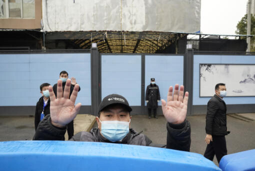 FILE - A security guard waves for journalists to clear the road after a convoy carrying the World Health Organization team entered the Huanan Seafood Market on the third day of a field visit in Wuhan in central China&rsquo;s Hubei province on Jan. 31, 2021. The hunt for COVID-19 origins has gone dark in China. An AP investigation drawing on thousands of pages of undisclosed emails and documents and dozens of interviews found feuding officials and fear of blame ended meaningful Chinese and international efforts to trace the virus almost as soon as they began, despite years of public statements to the contrary.