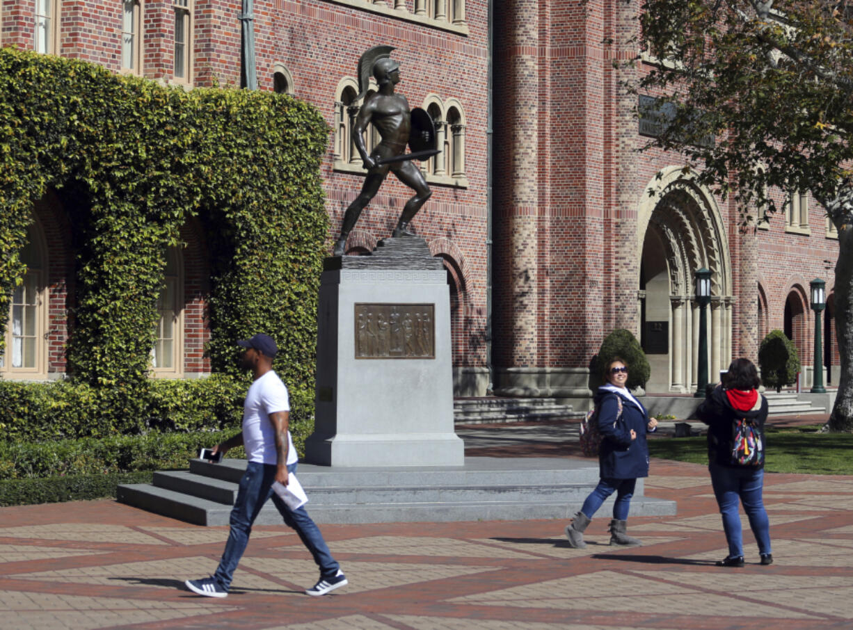 FILE - People pose for photos, March 12, 2019, in front of the iconic Tommy Trojan statue on the campus of the University of Southern California in Los Angeles. As more than 2 million graduating high school students from across the United States finalize their decisions on what college to attend this fall, many are facing jaw-dropping costs &mdash; in some cases, as much as $95,000.