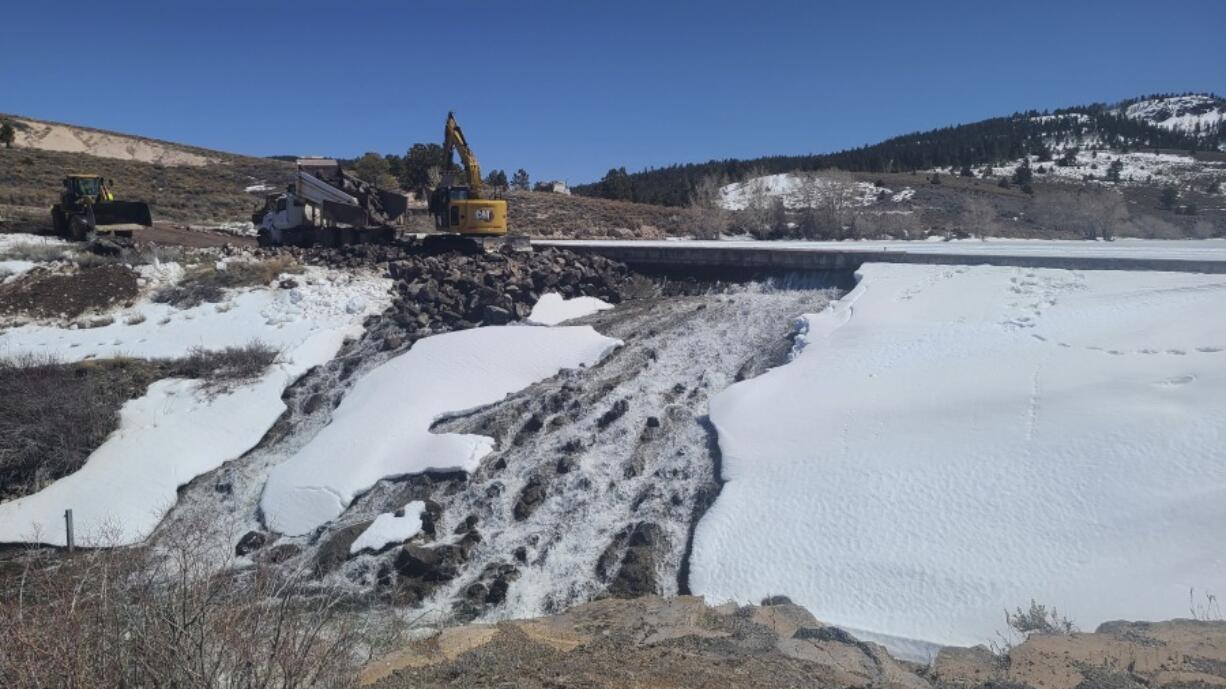 In this photo provided by the Utah Division of Water Rights, crews use heavy machinery to place boulders downstream of the cracked Panguitch Lake Dam to reinforce the wall, Wednesday, April 10, 2024, in Panguitch, Utah.