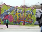 People walk by a mural in downtown Flint, Mich., Monday, March 25, 2024.