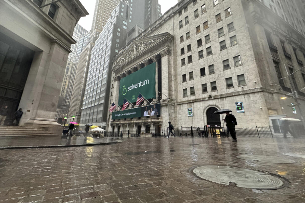 People walk past the New York Stock Exchange Wednesday, April 3, 2024 in New York. Healthcare business Solventum, shown on the banner, started trading at the NYSE on Wednesday.