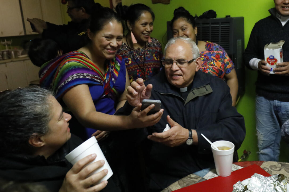 Cristel Cordona, second from left, shows photos of a recent marriage to visiting Guatemalan Cardinal Alvaro Ramazzini, at the St. Anne Catholic Church, in Carthage, Miss., Dec. 20, 2019. Ramazzini was at the parish to participate in a listening session with immigrants impacted by arrests by immigration agents at seven Mississippi food processing plants. (AP Photo/Rogelio V.
