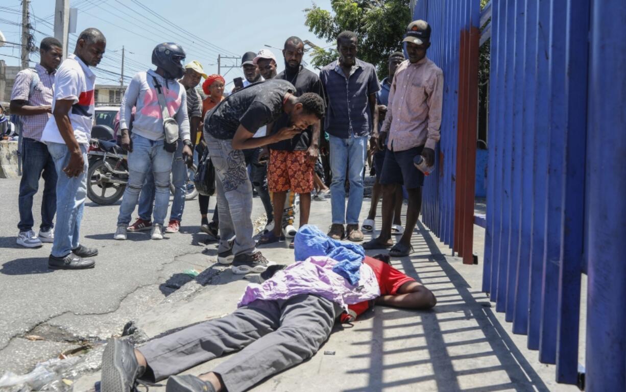 People observe the body of a man lying on the street of the Delmas 30 neighborhood in Port-au-Prince, Haiti, Monday, April 1, 2024. Witnesses reported that he was struck by a stray bullet during a shootout between police and gangs.