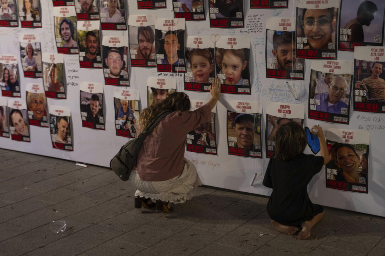 FILE - A woman touches photos of Israelis missing and held captive in Gaza, displayed on a wall in Tel Aviv on Oct. 21, 2023. One of the missing, Ohad Munder-Zichri, turned 9 on Monday. But instead of celebrating at home with his family and friends, he was somewhere in Gaza, one of more than 200 Israelis held hostage by Hamas since their devastating Oct. 7 incursion.