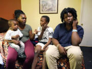 Ida Cartlidge, second from left, holds her youngest son Nolan while sitting with sons Amarii and Jakavien, right, on Nov. 29, 2023, in the middle of their two-bed motel room that serves as their temporary residence after a deadly tornado destroyed their home in March. The Cartlidge family of five spent nearly a year in the cramped motel room in search of a more permanent home, like many of their displaced neighbors. (AP Photo/Rogelio V.