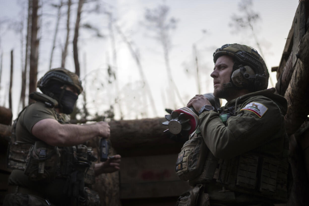 A Ukrainian serviceman from the Azov brigade known by call sign Chaos, right, carries mortar shell, while he waits for a command to fire, at positions of 122 mm HM 16 mortar around one kilometer away from Russian forces on the frontline in Kreminna direction, Donetsk region, Ukraine, Friday, April 12, 2024.