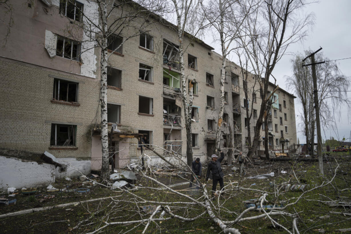 FILE - Local men cut trees in front of a residential building that was heavily damaged by a Russian airstrike in Lukiantsi, Kharkiv region, Ukraine, on Tuesday, April 16, 2024.