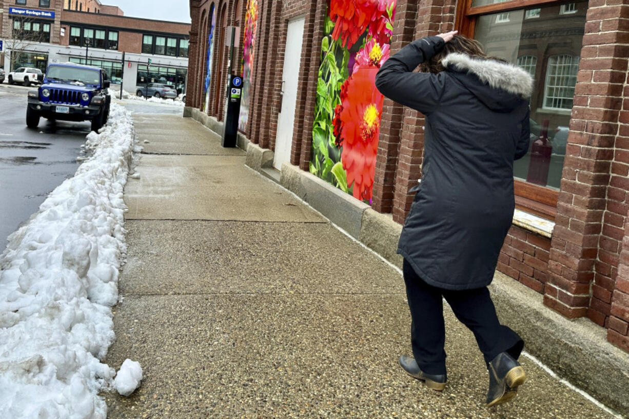 A woman walks past a photographic mural depicting colorful flowers in Concord, N.H., Friday, April 5, 2024, a day after a Spring storm dumped snow across the region.