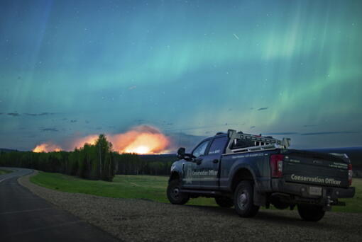 This photo provided by the Ministry of Water, Land and Resource Stewardship shows a wildfire,  Aurora Borealis  overhead, near Fort Nelson, British Columbia Saturday, May 11, 2024. An intense wildfire could hit a town in western Canada on Monday, based on forecasts of strong winds that have been fueling the out-of-control blaze which has already forced the evacuation of thousands, fire experts and officials warned.