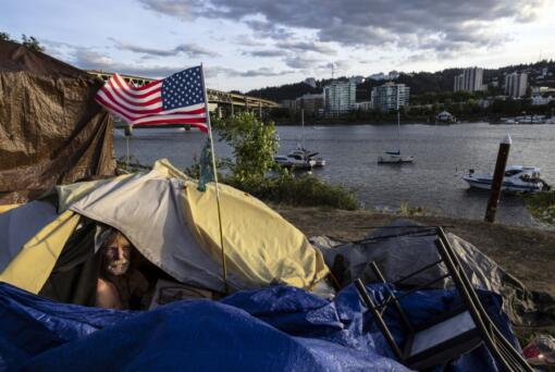 FILE - Frank, a homeless man sits in his tent with a river view in Portland, Ore., Saturday, June 5, 2021. The city council in Portland, Oregon, has approved new homeless camping rules. Under the rules, people who reject offers of shelter can face penalties, including fines of up to $100 or up to seven days in jail.