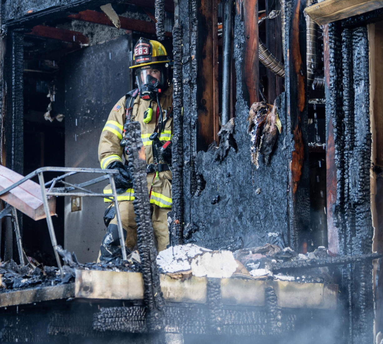 A firefighter stands near the back patio of a burned apartment unit June 11 at the site of a three-alarm fire at the Erica Village apartment complex in Hazel Dell. Regional fire officials are sounding the alarm over a disturbing trend at the start of summer: a rash of destructive fires at multifamily buildings.