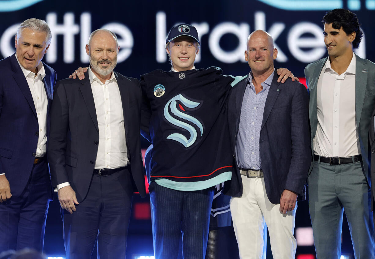 Berkly Catton, center, poses after being selected by the Seattle Kraken during the first round of the NHL hockey draft Friday, June 28, 2024, in Las Vegas.