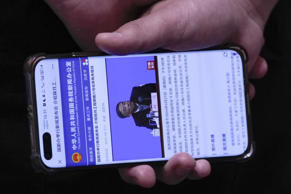 A staff member holding a smartphone showing the State Council Information Office website broadcasting a live of Hu Hao, chief designer of China&rsquo;s Chang&rsquo;e 6 probe speaking during a press conference at the State Council Information Office in Beijing, Thursday, June 27, 2024. China&rsquo;s space officials said Thursday they welcomed scientists from across the world to apply to study the lunar rock samples the Chang&rsquo;e 6 probe brought back to earth in a historic mission, but noted there were limits to that cooperation, specifically with the U.S.