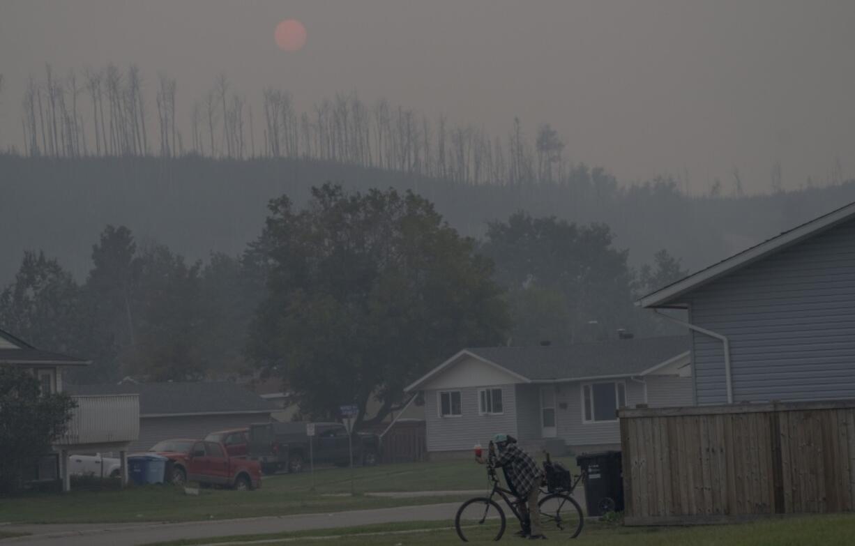 FILE - A person rides a bicycle on a smokey day due to wildfires in Fort McMurray, Canada, Sep. 2, 2023. Catastrophic Canadian warming-fueled wildfires last year pumped more heat-trapping carbon dioxide into the air than India did by burning fossil fuels, new research found. (AP Photo/Victor R.