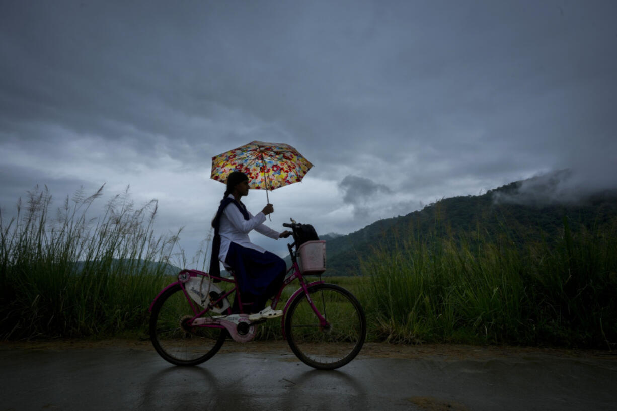 A school girl with an umbrella rides on her bicycle to school June 20 during the monsoon rain as clouds hover over the sky on the outskirts of Guwahati, India.